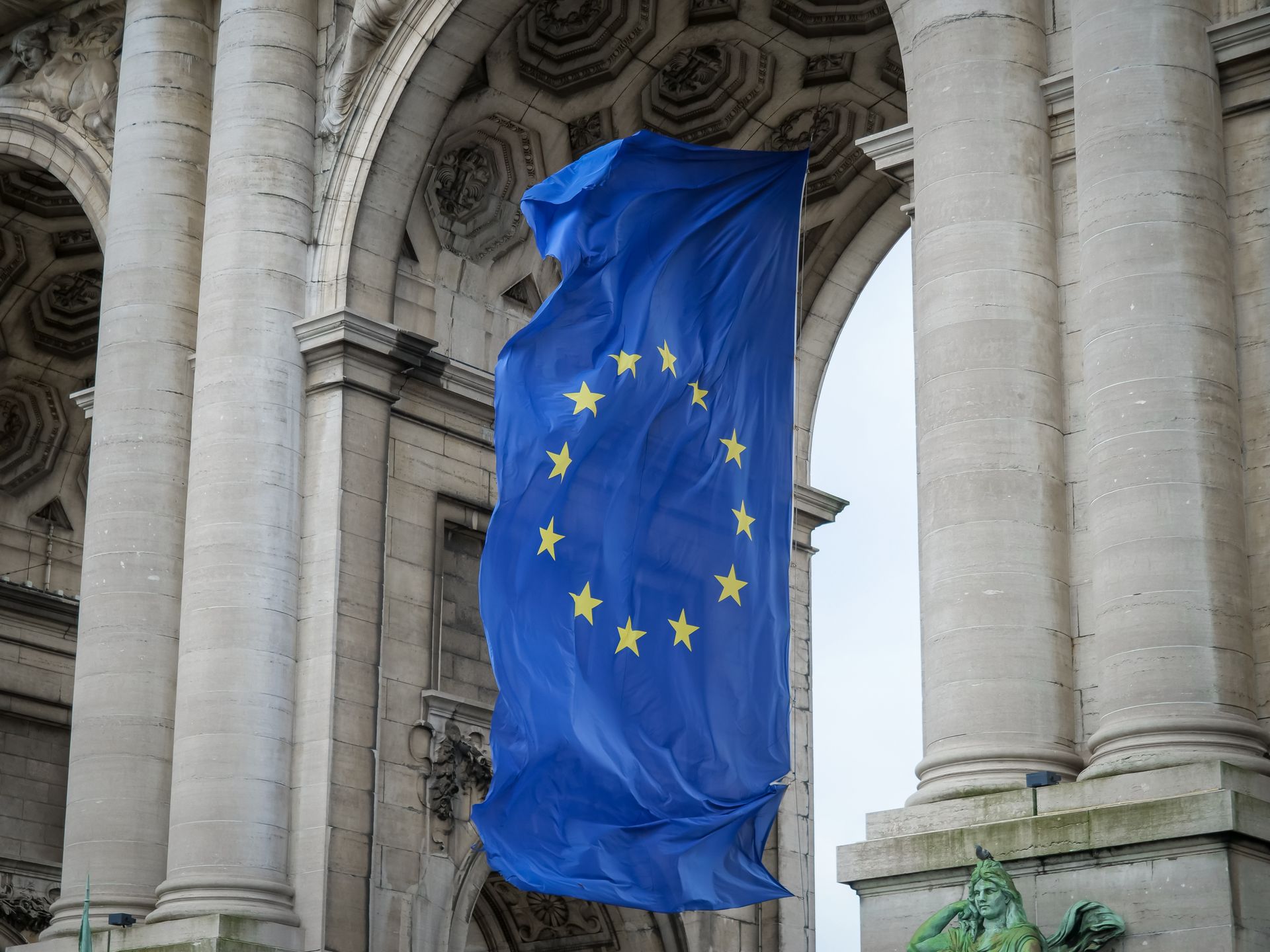 The European Union flag flying between the stone arches of a colonnade